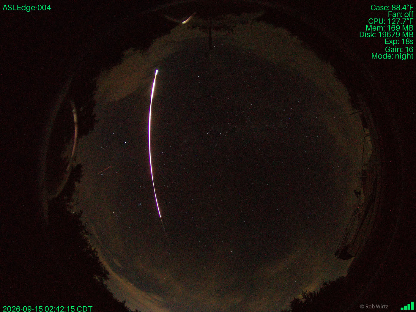 A fisheye all-sky exposure from an AllSkyLabs field-test camera showing the entire night sky, with a bright streak crossing the frame. Telemetry burned into the image reads ASLEdge-004, Exp: 18s, Gain: 16, Mode: night, 2026-09-15 02:42:15 CDT.